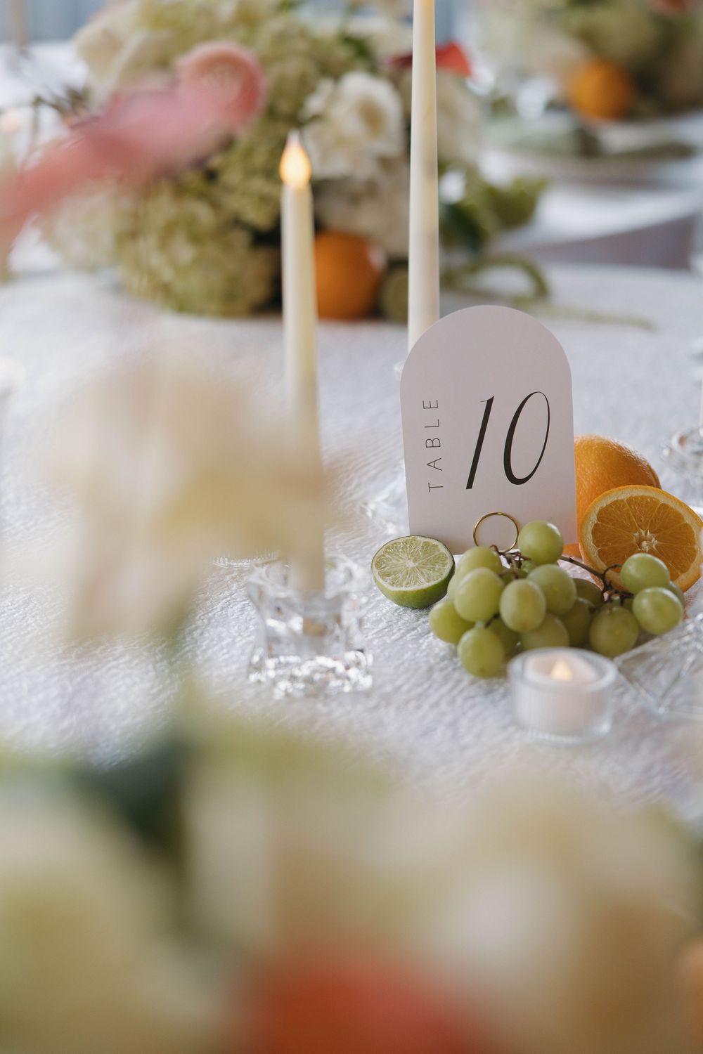 Elegant table setting with lit candles, fresh green grapes, and acrylic table number markers creating a soft romantic ambiance.