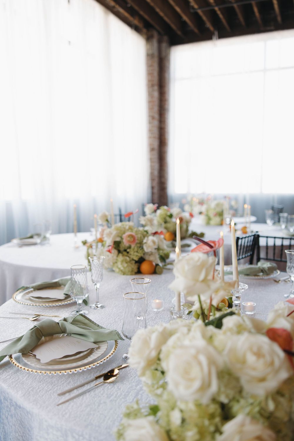 Elegant wedding reception table settings with crystal charger plates and delicate white floral centerpieces in a bright venue.