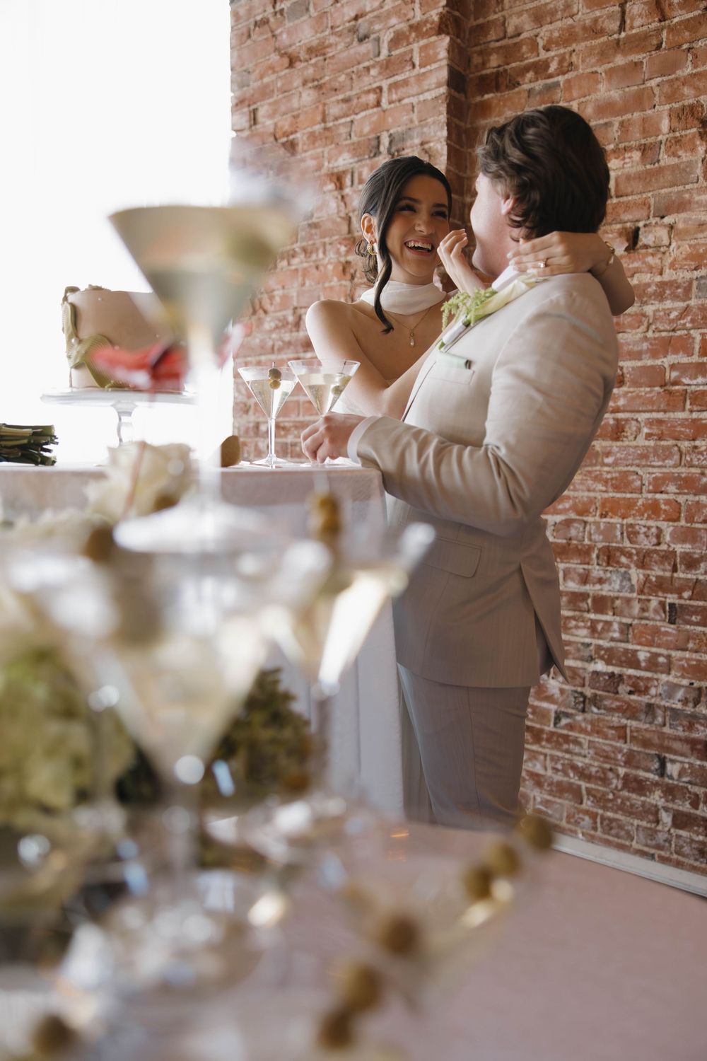 Two people share a joyful moment together against an exposed brick wall backdrop during a formal event.
