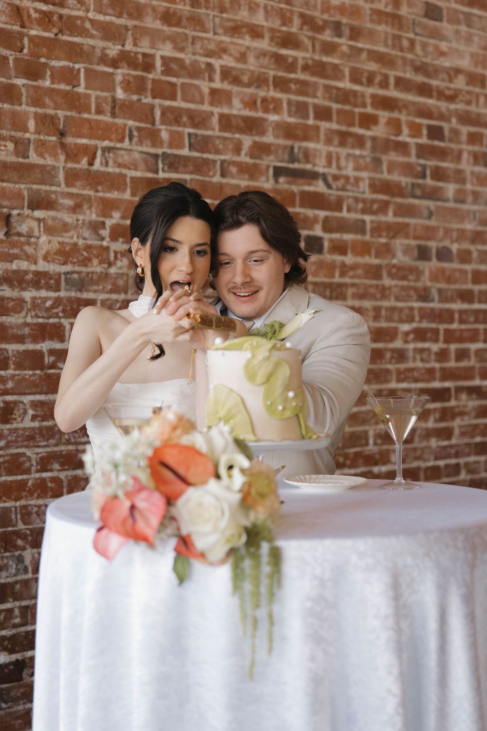 A happy couple shares a joyful moment together at a reception table decorated with floral arrangements and a white tablecloth.