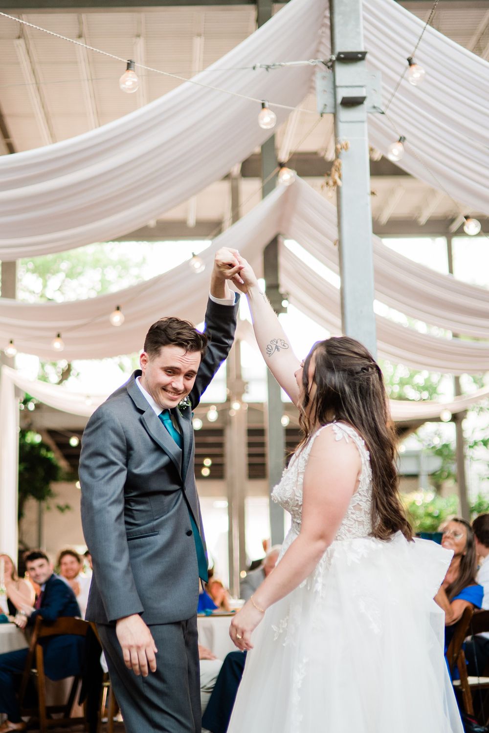 Wedding couple dancing under draped white fabric and string lights at an outdoor reception venue.