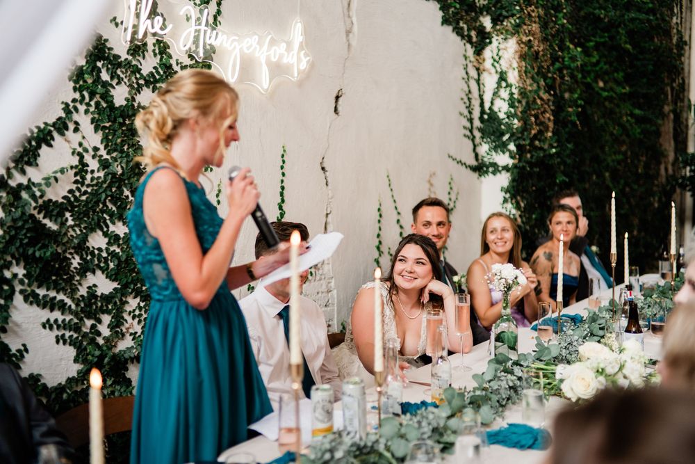 A wedding reception scene with bridesmaids in teal dresses seated at a decorated table.