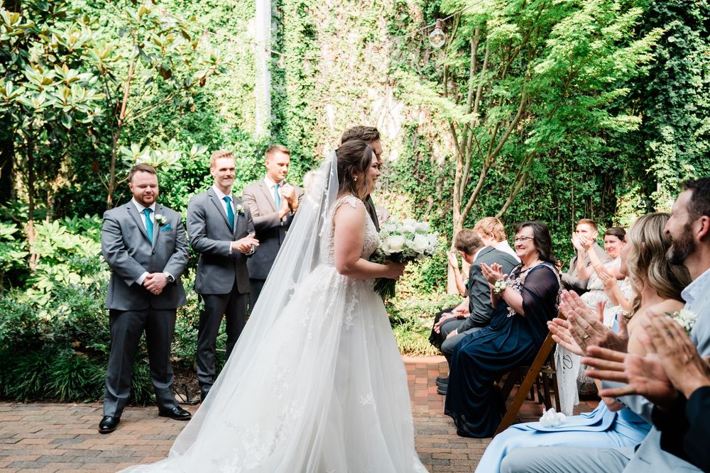 Wedding ceremony in a lush garden setting with guests watching a couple exchange vows beneath greenery.
