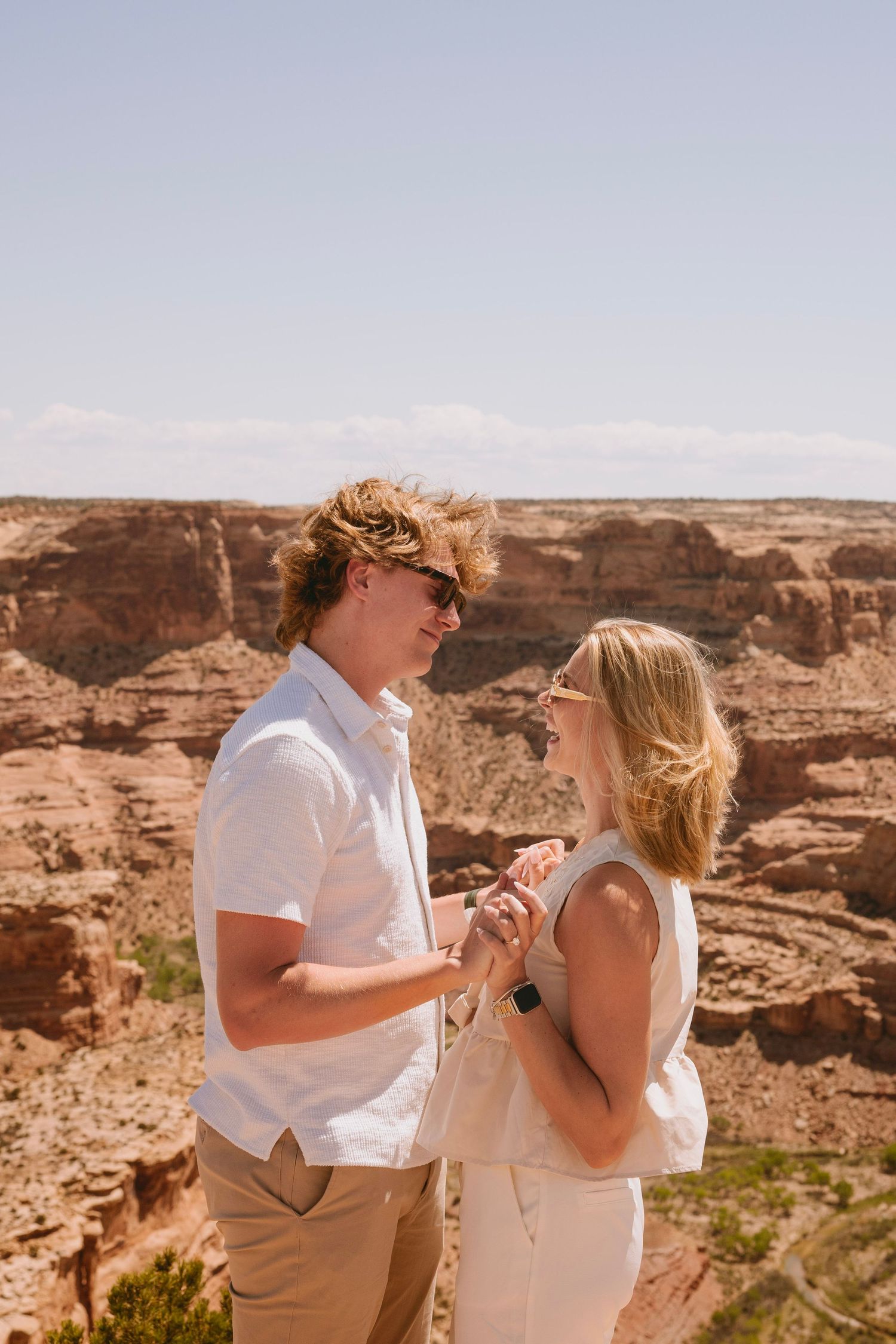 A couple shares an intimate moment at the edge of a scenic canyon with red rock formations stretching to the horizon.