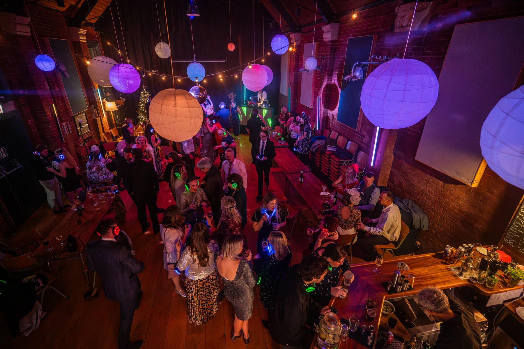 Event space decorated with illuminated paper lanterns overhead while guests gather for a celebration at night.