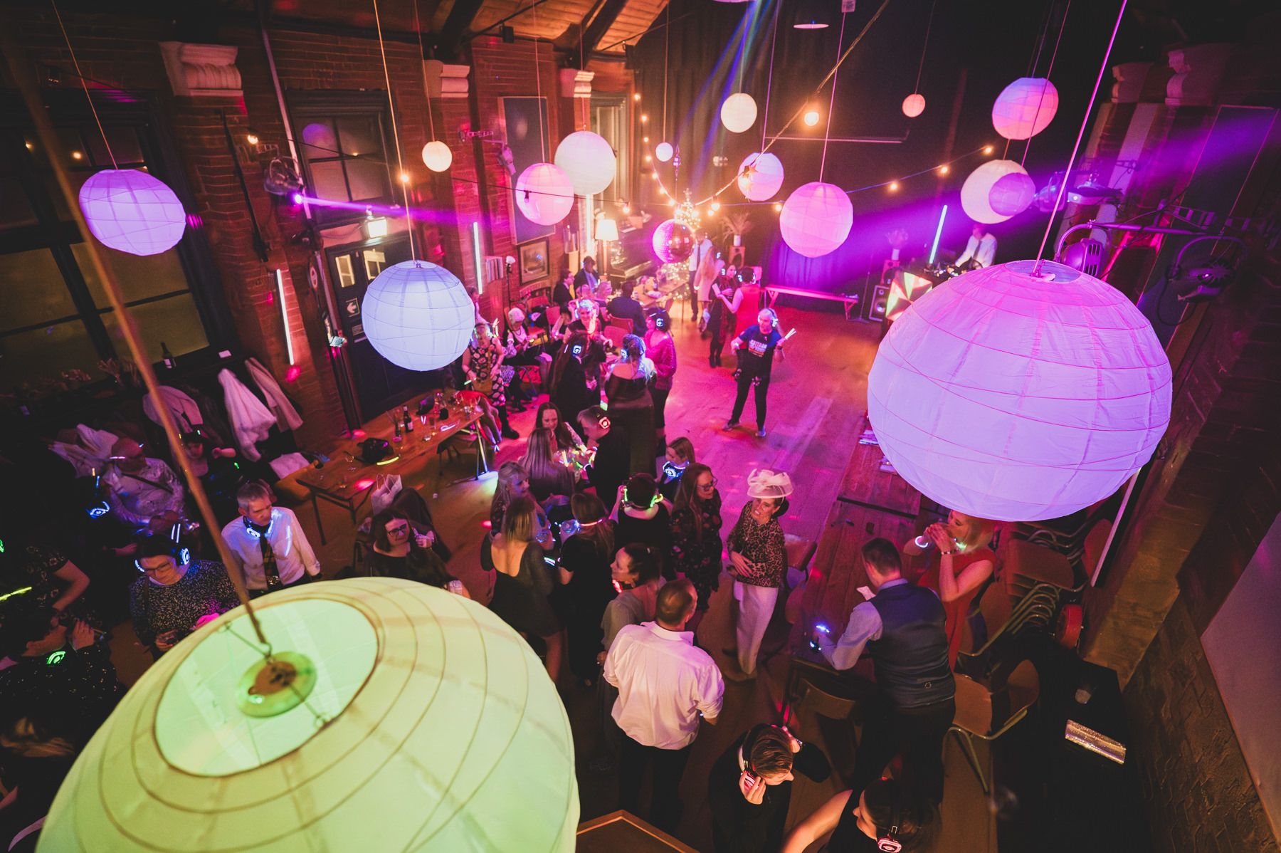 Overhead view of a lively reception venue with glowing paper lanterns and purple lighting illuminating dancing guests.