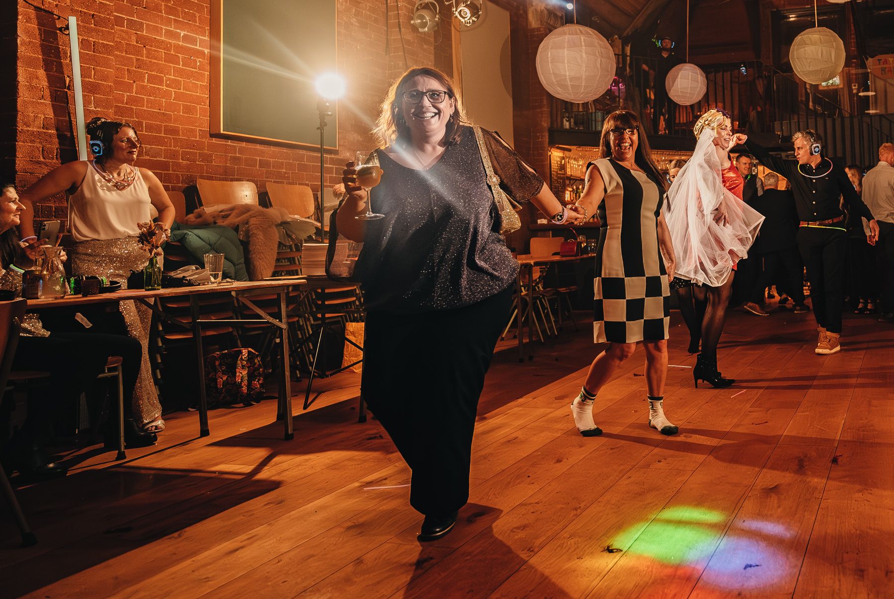 Dance party attendees enjoying themselves on a hardwood floor under warm lighting and paper lanterns in a vintage venue.