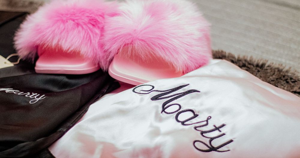 A pair of fluffy pink slippers next to a folded white pajama top on a textured brown carpet.