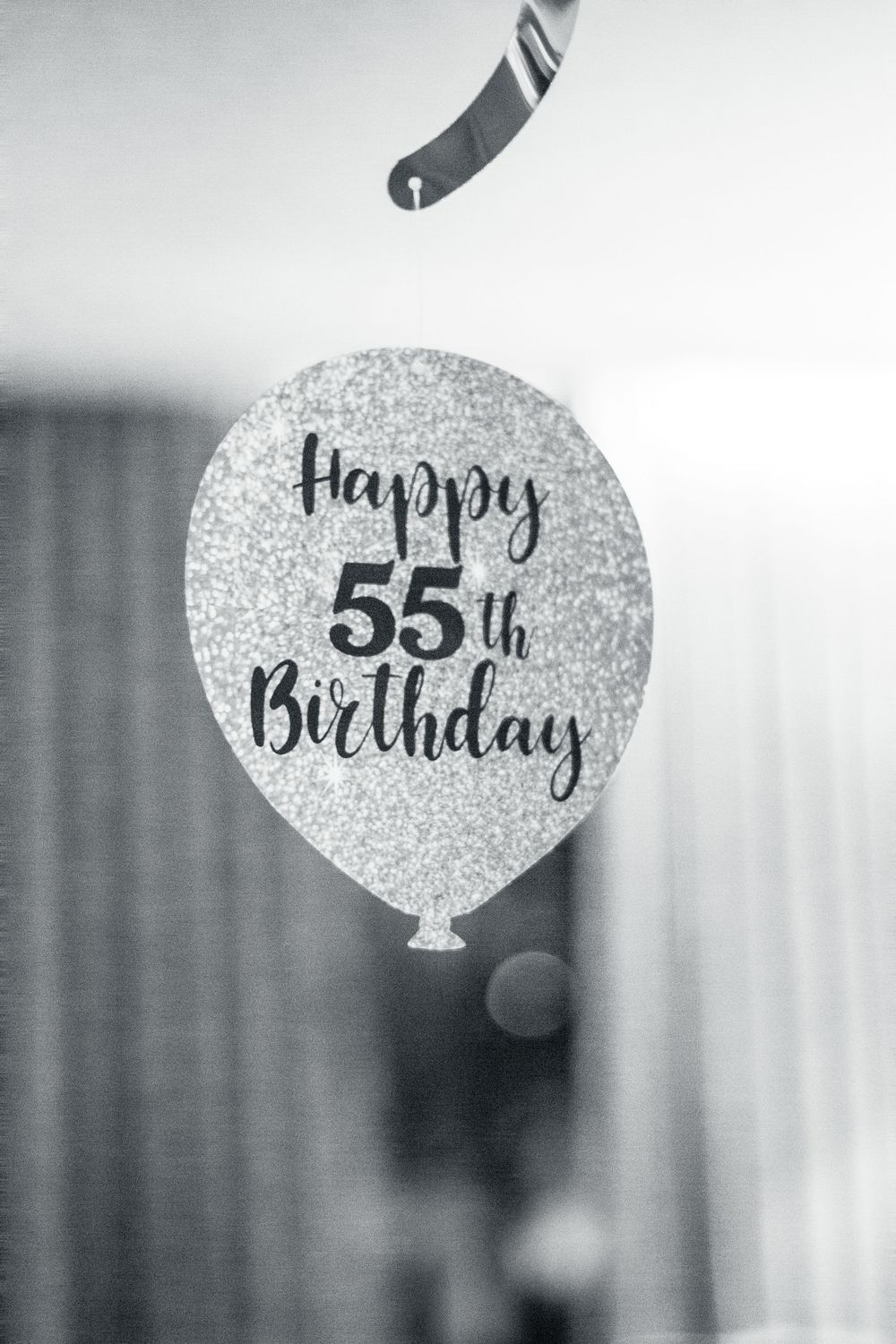 Glittery silver '55th Happy Birthday' decorative party tags hanging in a row against a blurred background.