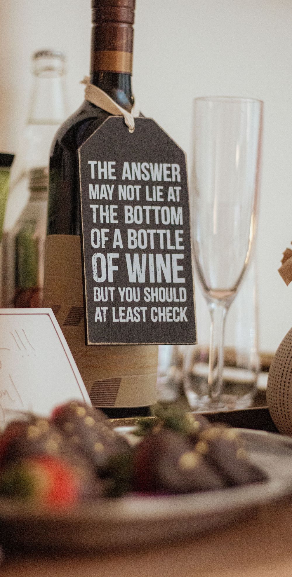 Wine bottle tags display humorous quotes about finding answers at the bottom of wine bottles at an elegant table setting.