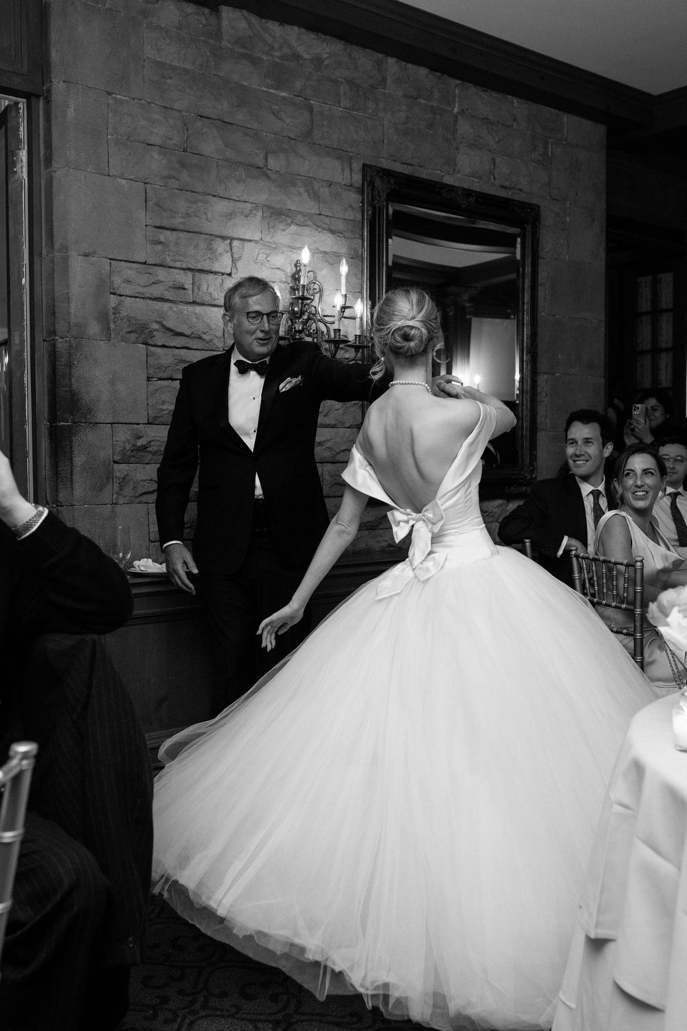 A black and white wedding photo showing a graceful bride in a full tulle gown being helped through an elegant doorway.