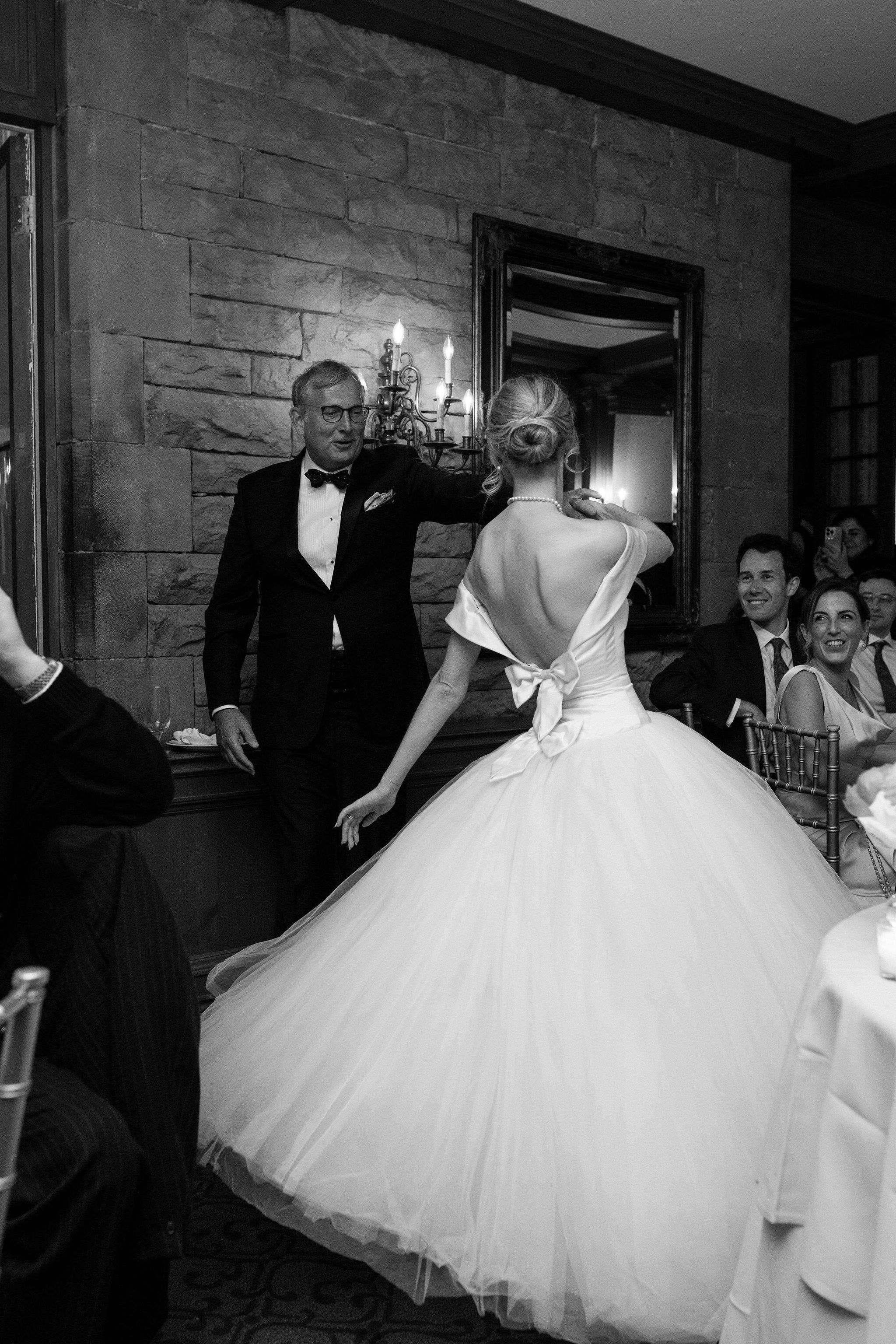 A black and white wedding photo showing a graceful bride in a full tulle gown being helped through an elegant doorway.