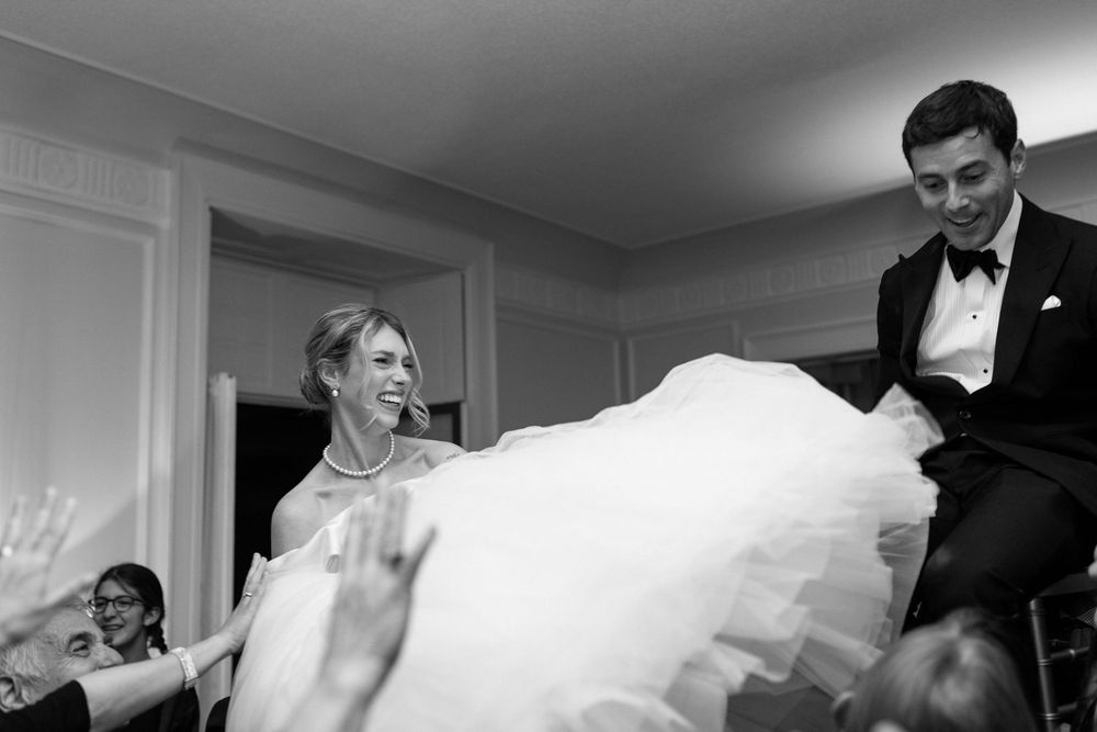 Black and white photo of a wedding couple laughing and dancing together during a celebration.