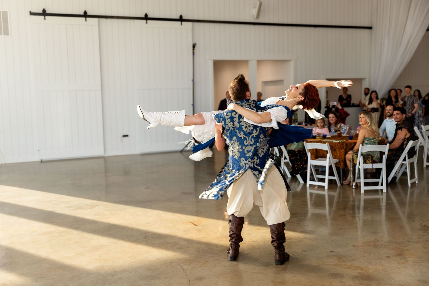 Dance performance in a white-walled venue with audience members seated in white chairs watching the performers.