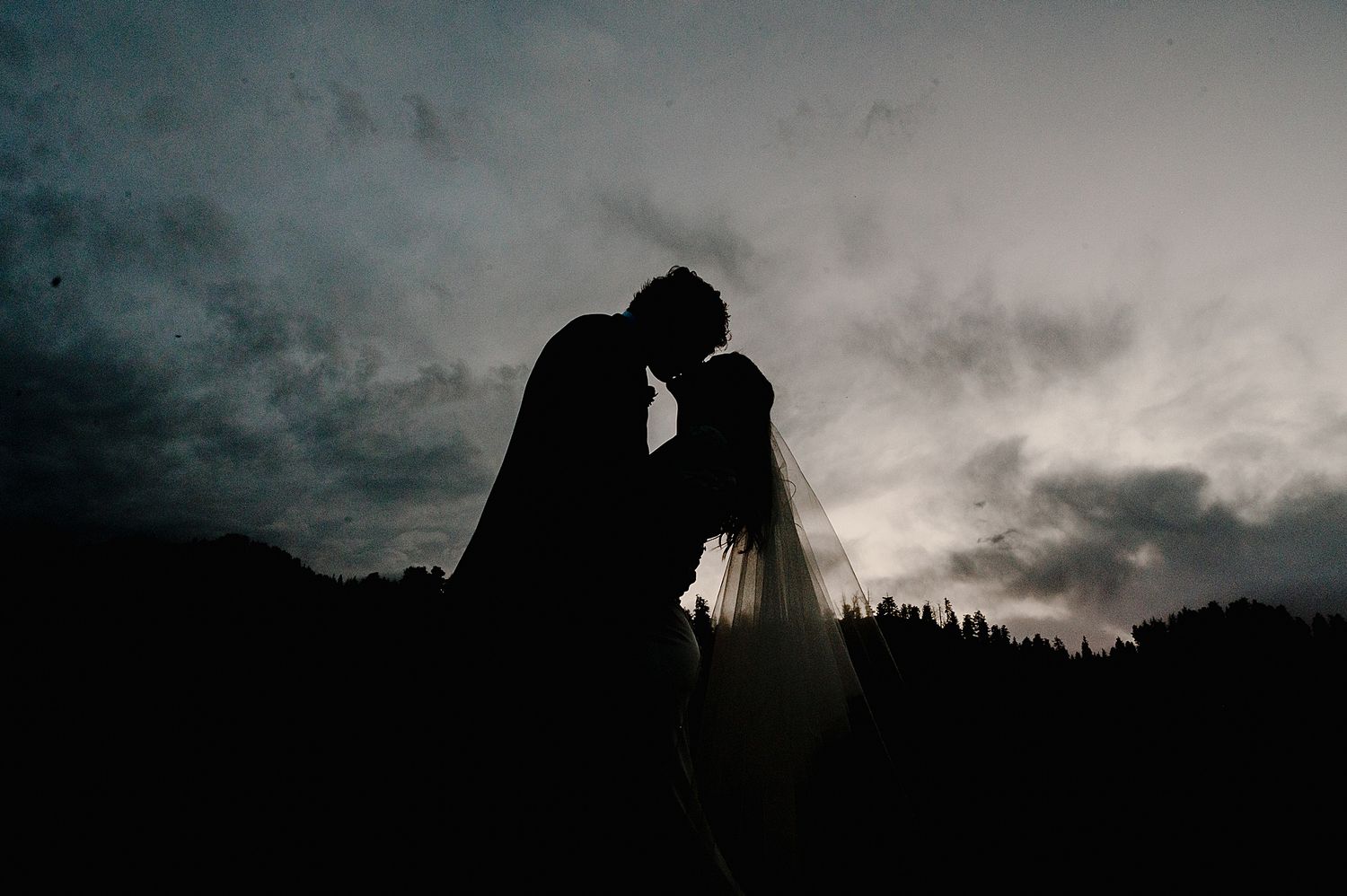 Silhouettes of couples embrace against a dramatic cloudy sunset sky creating romantic atmospheric scenes.
