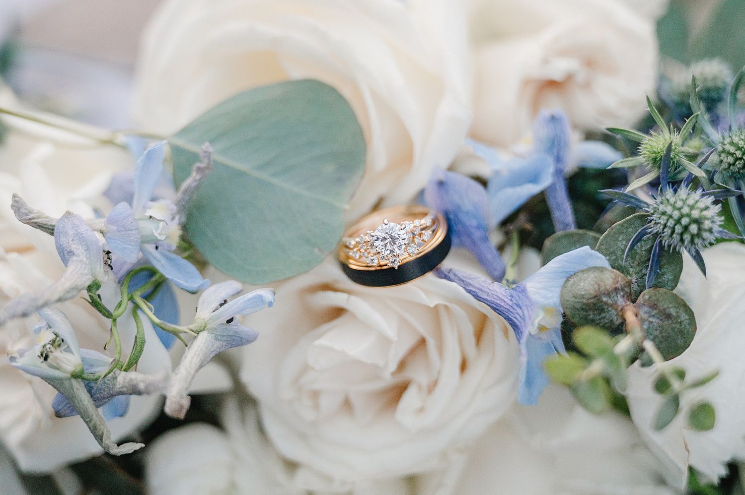 Gold wedding ring nestled among white roses and delicate blue flowers in a romantic floral arrangement.