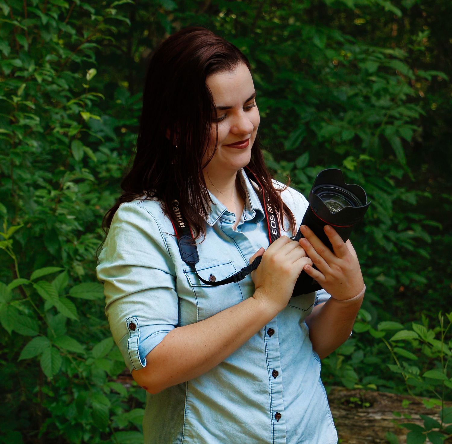Someone wearing a light denim shirt demonstrates camera equipment in a lush green outdoor setting.