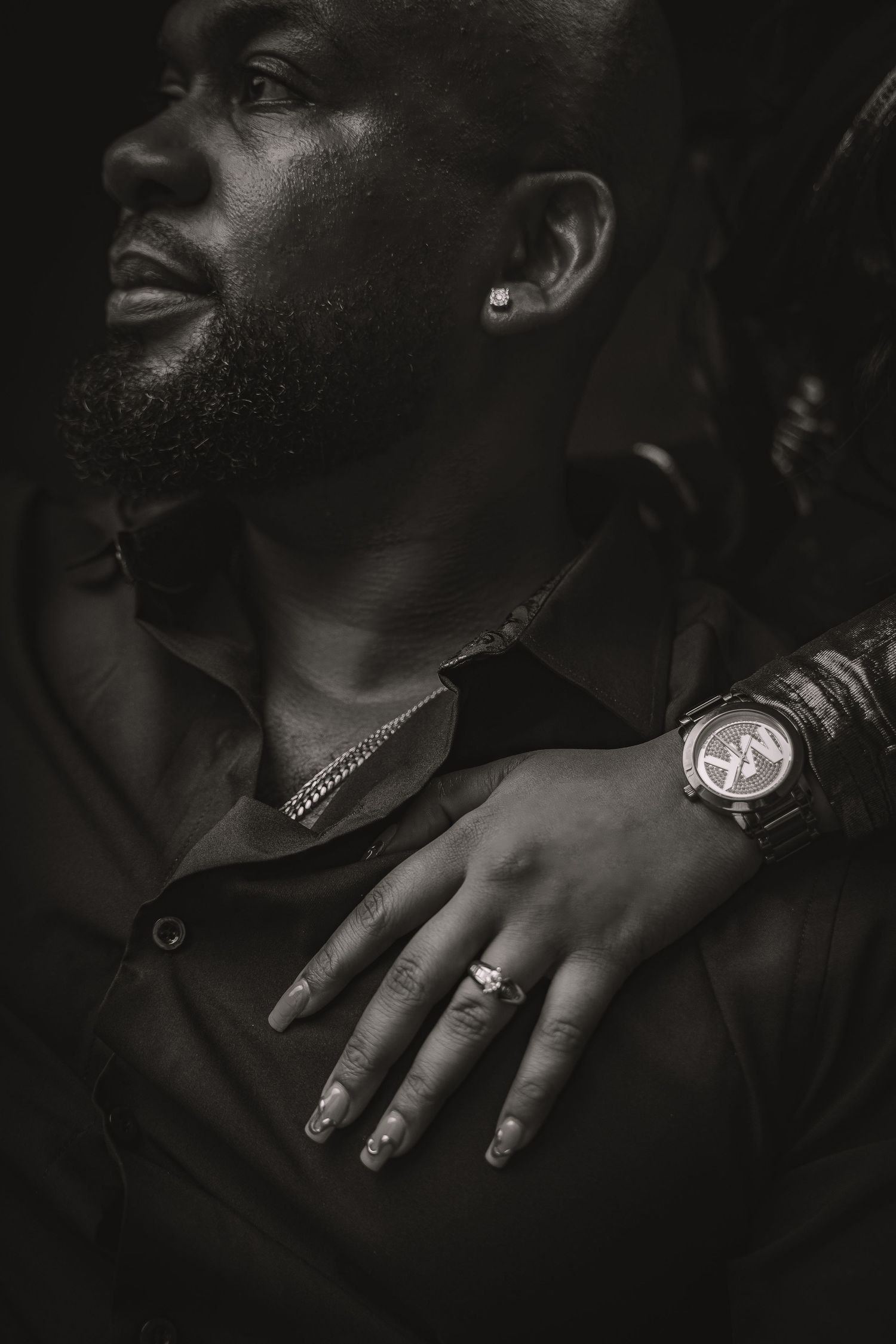 Close-up black and white shot of hands with decorative rings and jewelry against dark background.