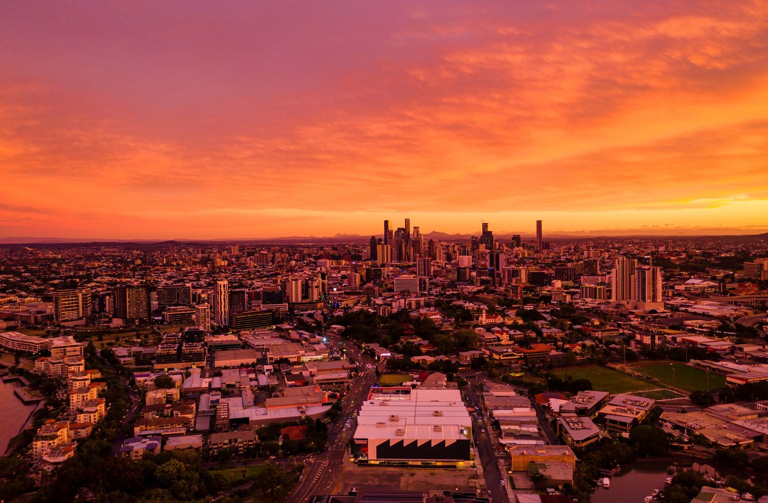Dramatic orange sunset illuminates a cityscape with tall buildings and modern architecture against a fiery sky.