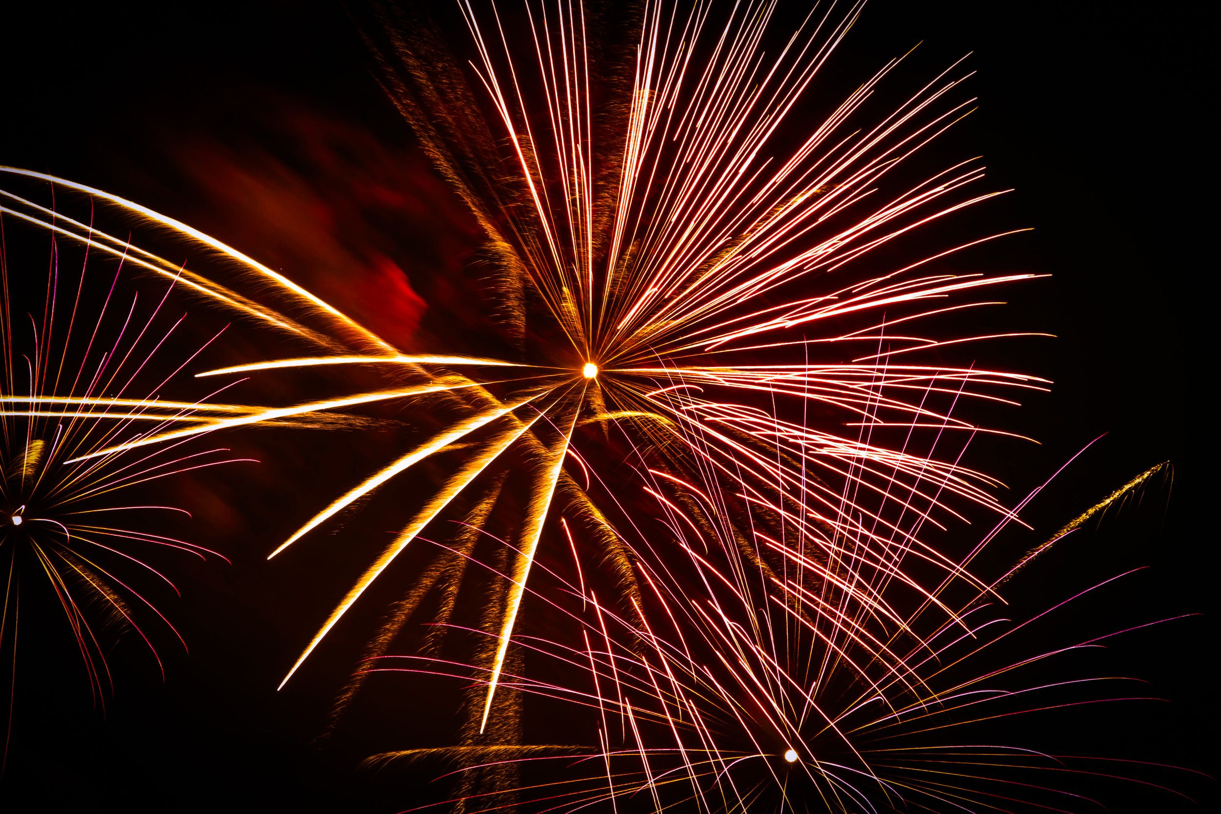 Vibrant red and gold fireworks burst across a dark night sky in a dazzling pyrotechnic display.