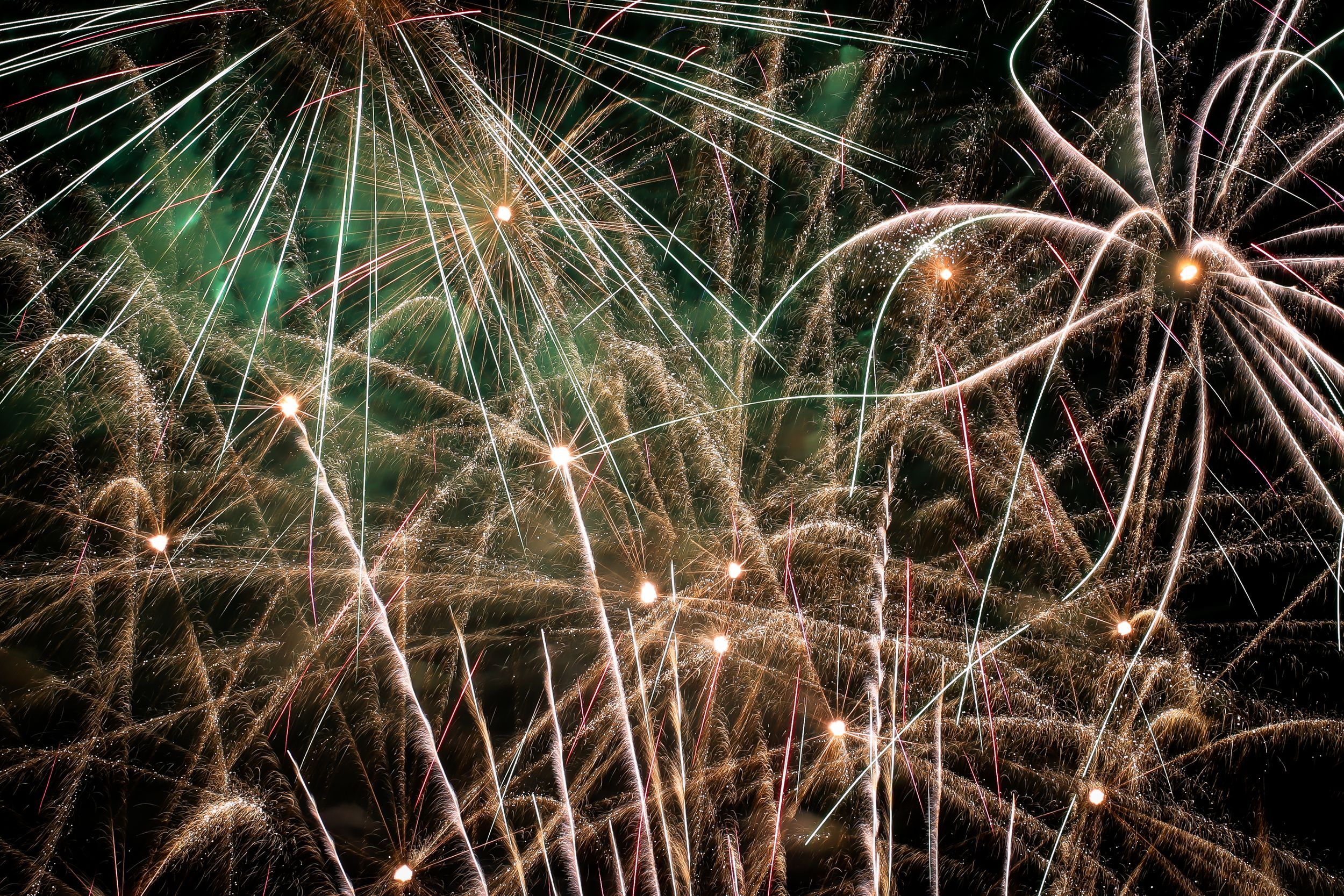 Vibrant bursts of green and gold fireworks illuminate the dark night sky during a festive pyrotechnic display.