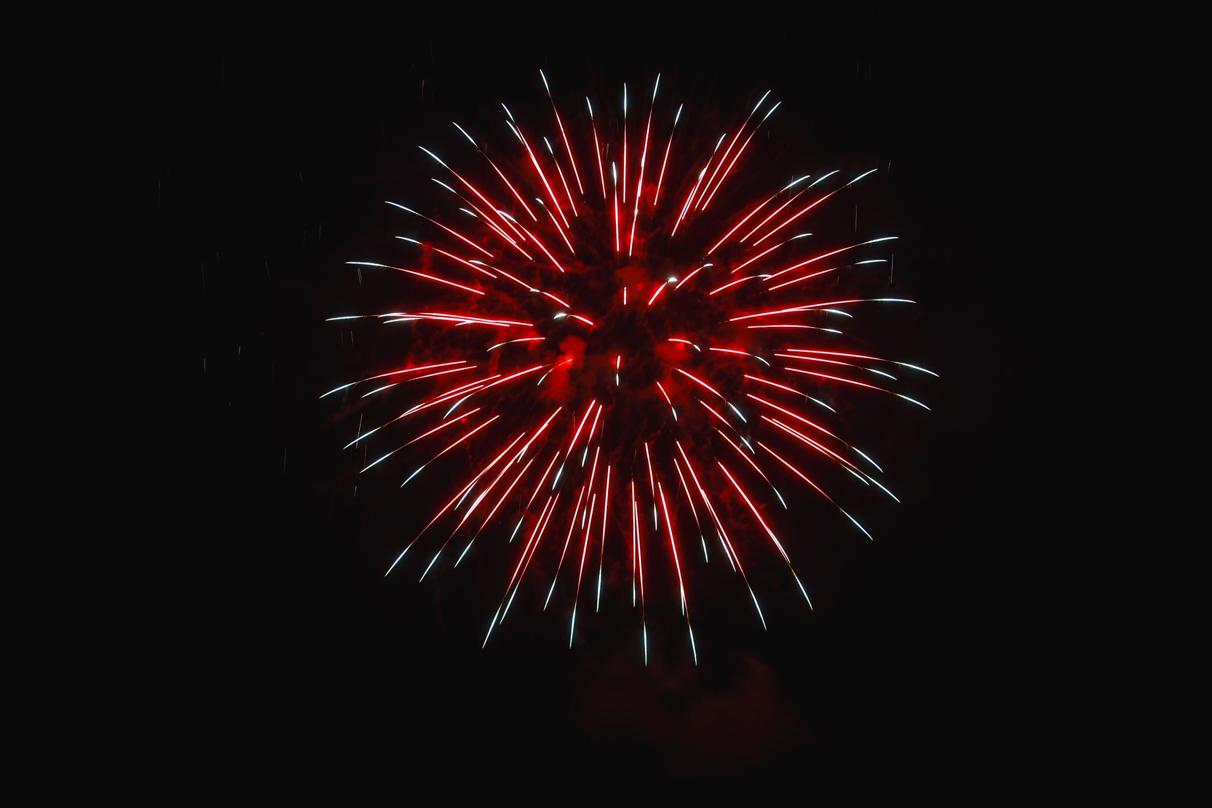 A bright red firework explosion lights up the dark night sky with radiating streaks and sparkles.