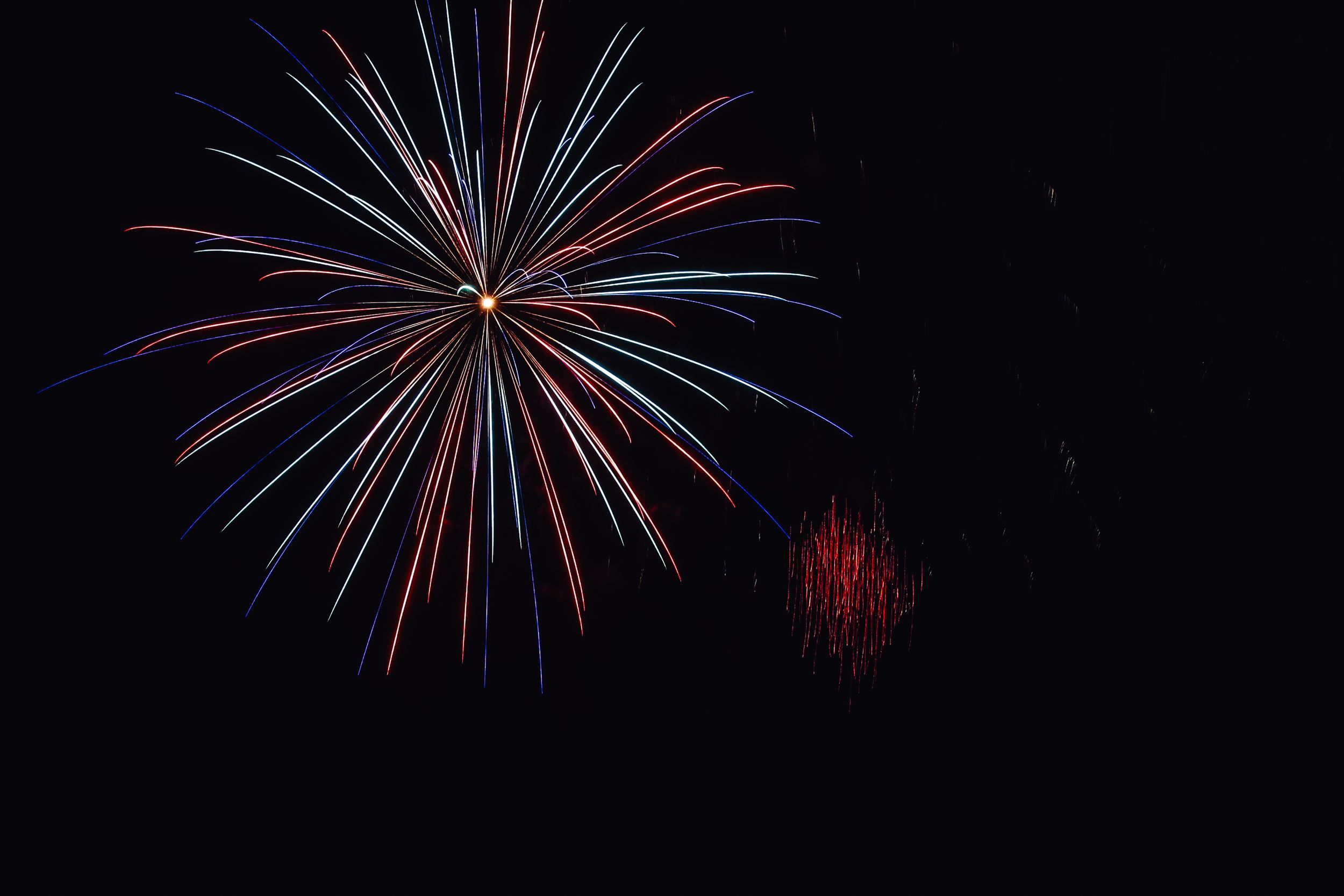 Red and blue fireworks burst across a dark night sky creating a patriotic display of colorful pyrotechnics.