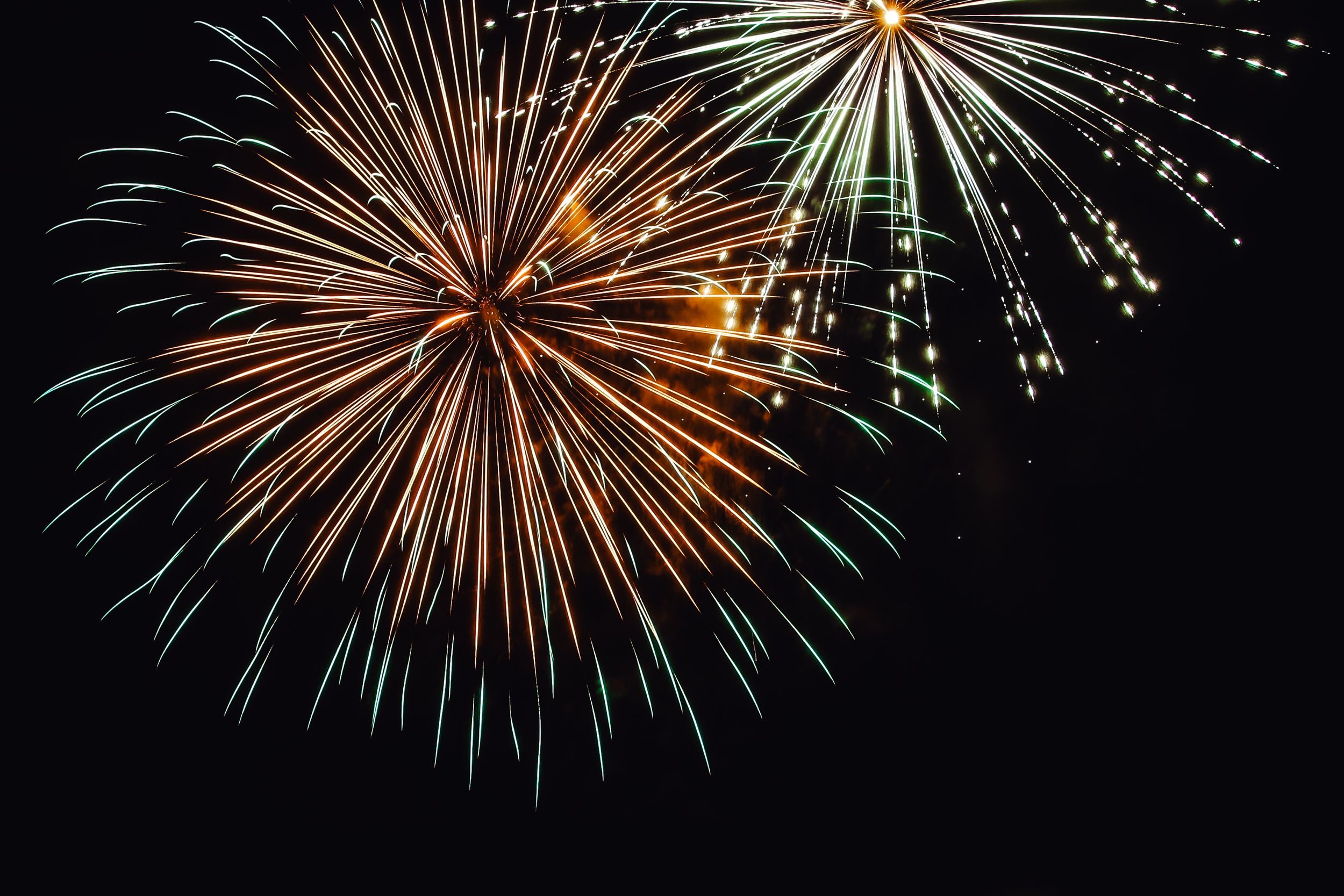 Vibrant fireworks display bursting in the night sky with orange and green sparks against dark background.