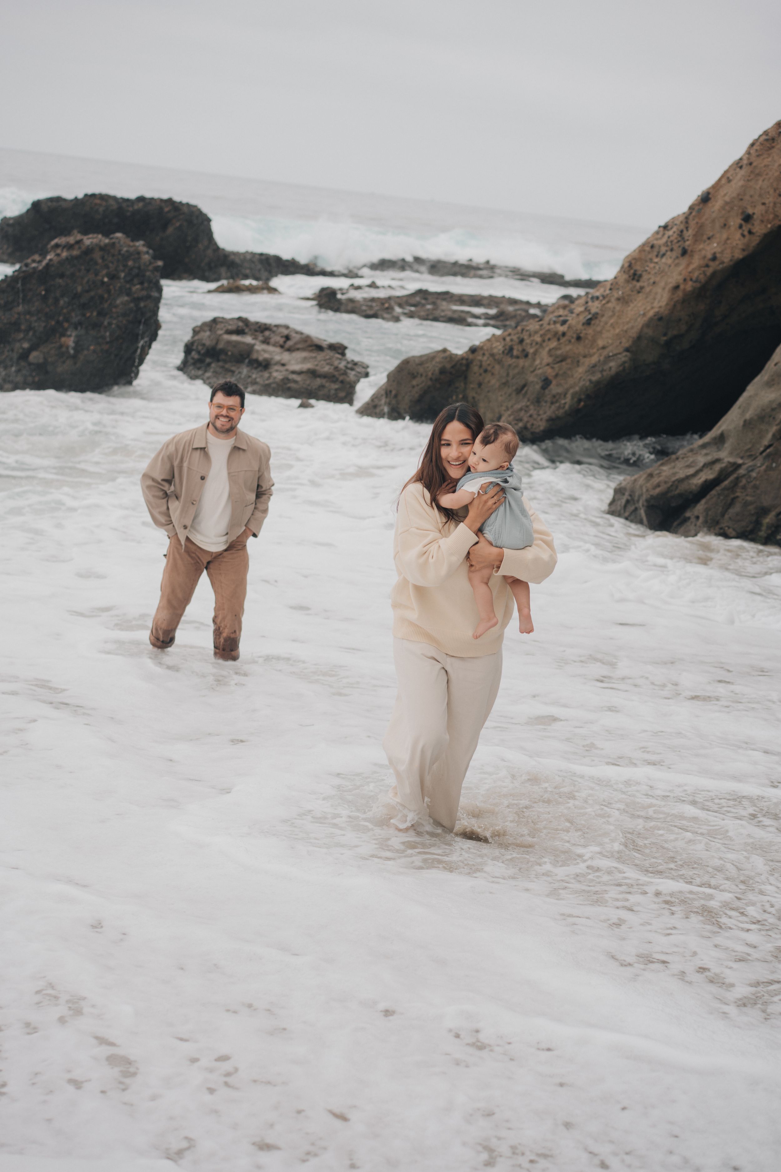 A family stands together on a beach with rocky outcrops during a misty overcast day.