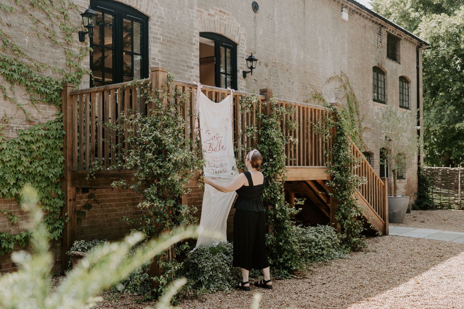a wedding stylist is hanging up a cloth welcome sign at the front of a wedding venue.