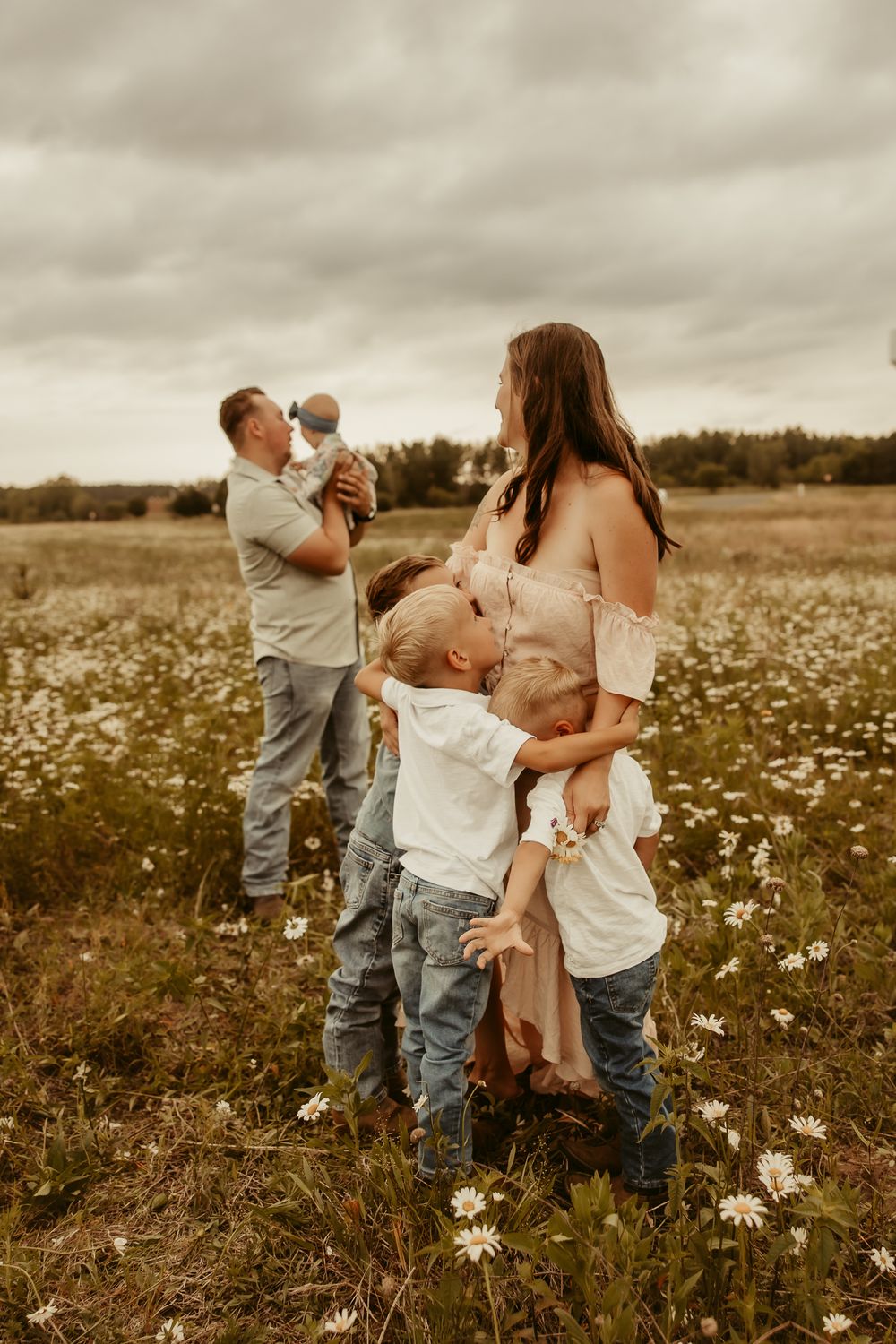 A family shares tender moments together in a sunlit field of white wildflowers during a lifestyle photoshoot Pine City Minnesota