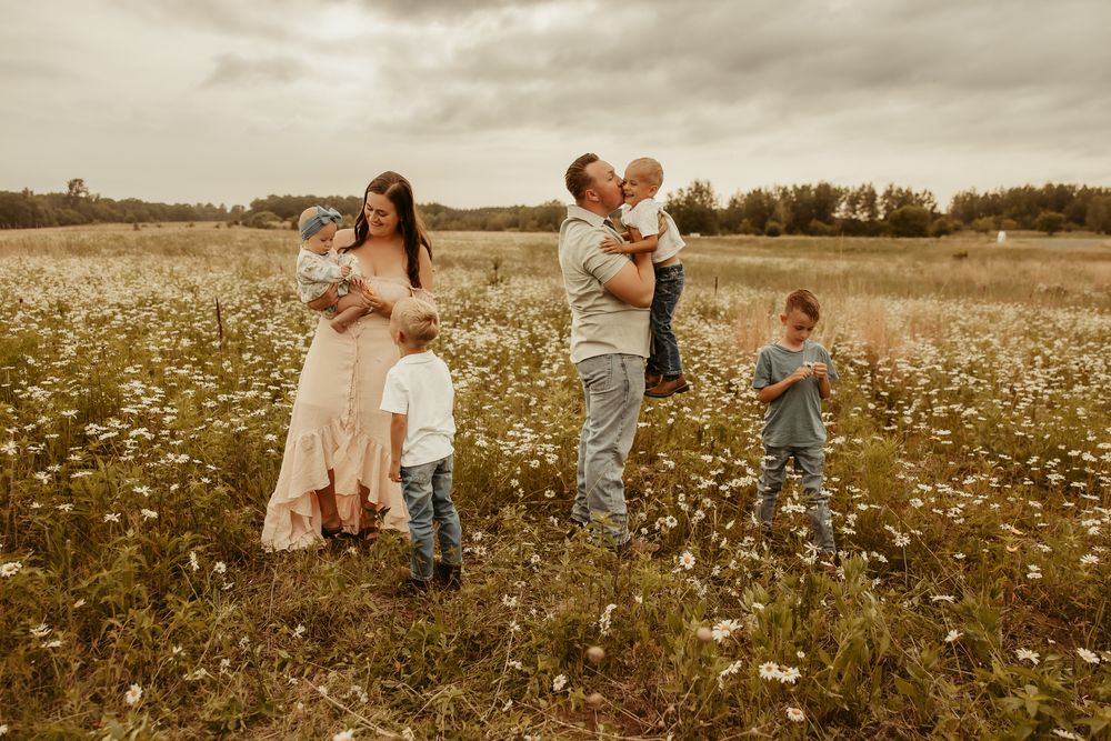 A family stands together in a wildflower meadow at sunset with ethereal golden light and a moody sky behind them. Pine City Minnesota