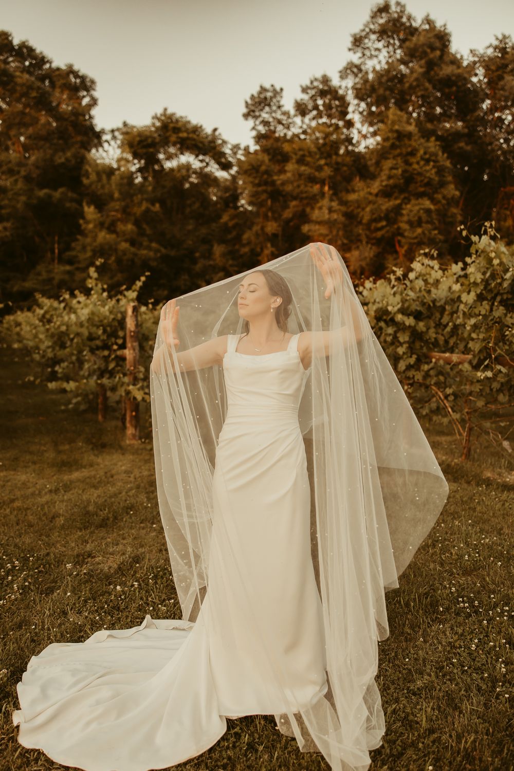 Ethereal wedding dress and flowing veil catch golden sunlight in an outdoor garden setting at sunset.Cottage Grove Minnesota