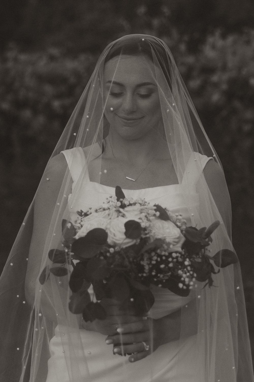 A bride wearing a traditional white wedding dress and veil holds a monochrome bouquet in this black and white photo Cottage Grove Minnesota