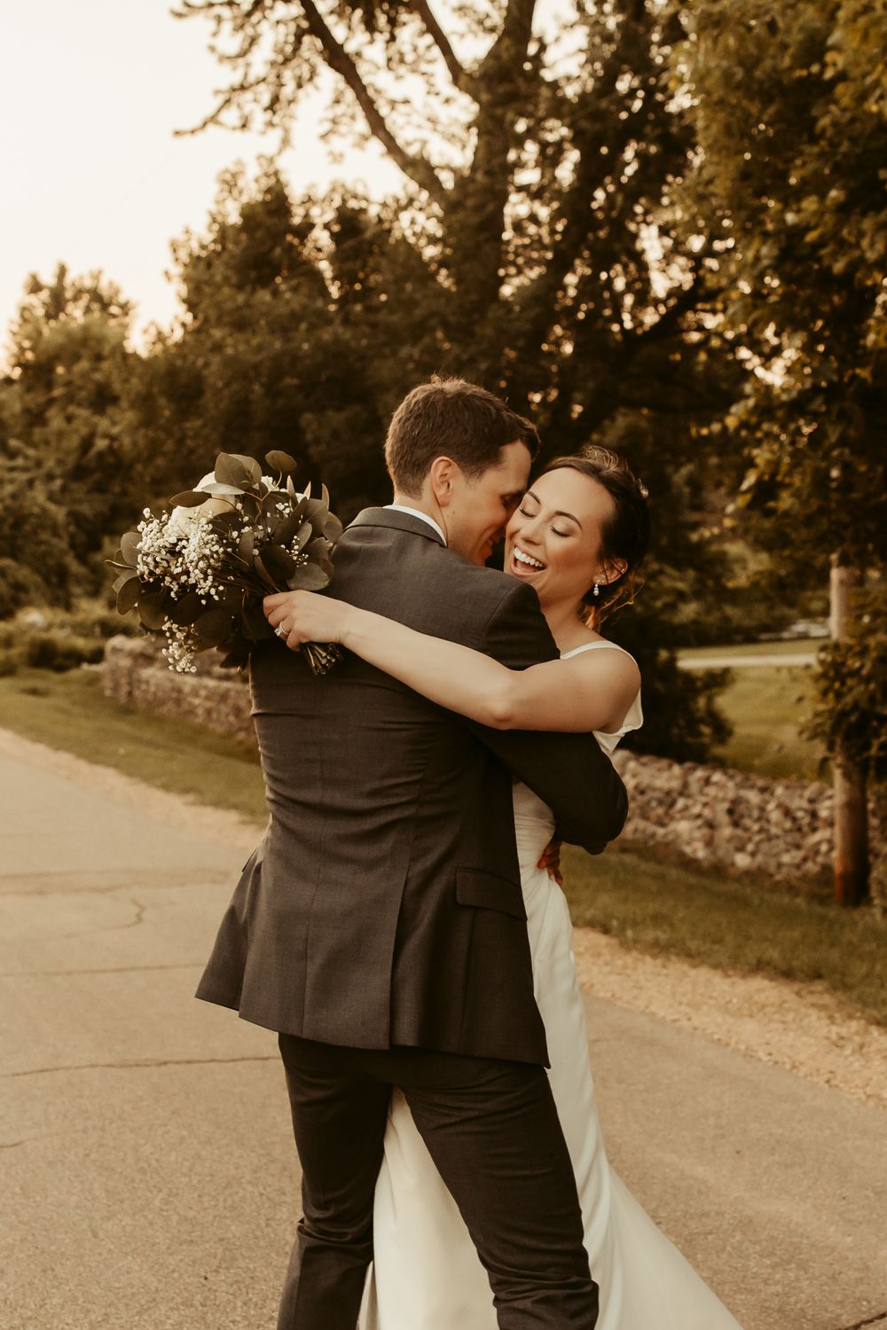 A newlywed couple embraces joyfully during a sunset photoshoot on a tree-lined path.
Cottage Grove Minnesota