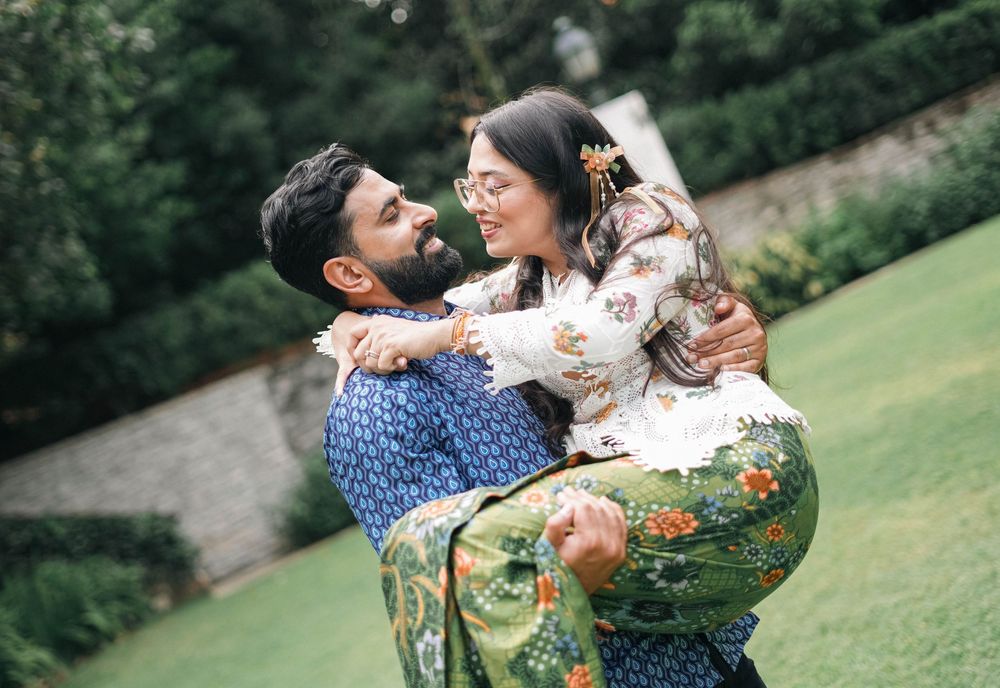 A joyful couple embraces and laughs together on a grassy lawn while wearing colorful patterned outfits.
