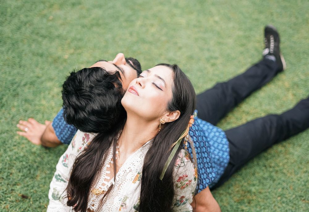 A joyful couple lying on grass laughing together while wearing coordinated blue and floral outfits.