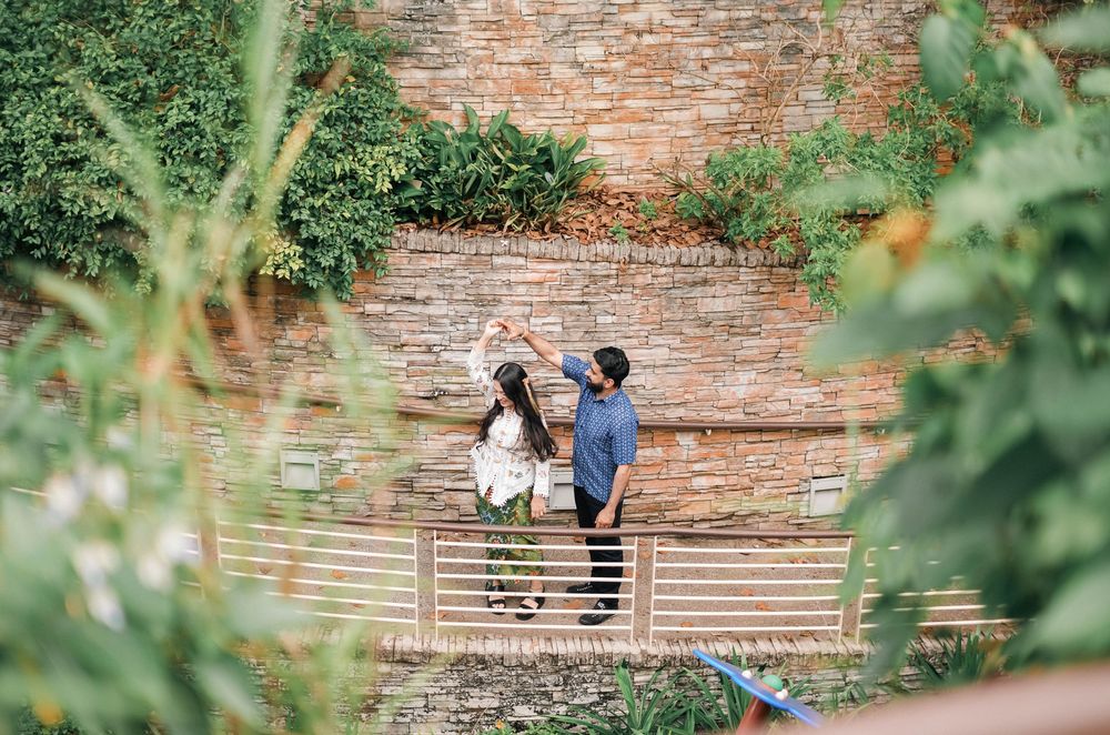 Two people share a romantic moment on stone steps surrounded by greenery and a rustic brick wall.