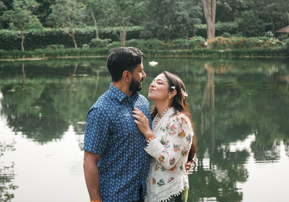 A romantic couple in a floral dress and blue shirt share a tender moment on a dock by a serene lake.