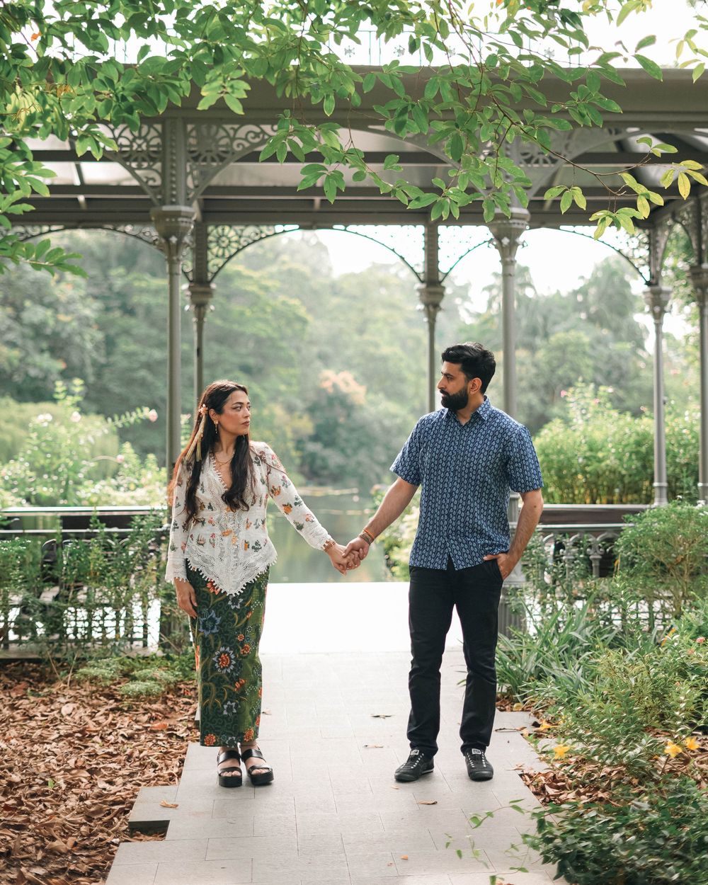 A couple walking hand in hand along a garden pathway under a covered walkway with leafy foliage.