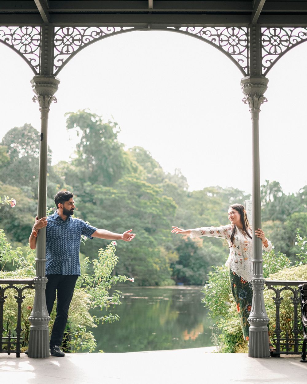 A romantic couple shares a tender moment on a decorative wooden gazebo overlooking a scenic lake.