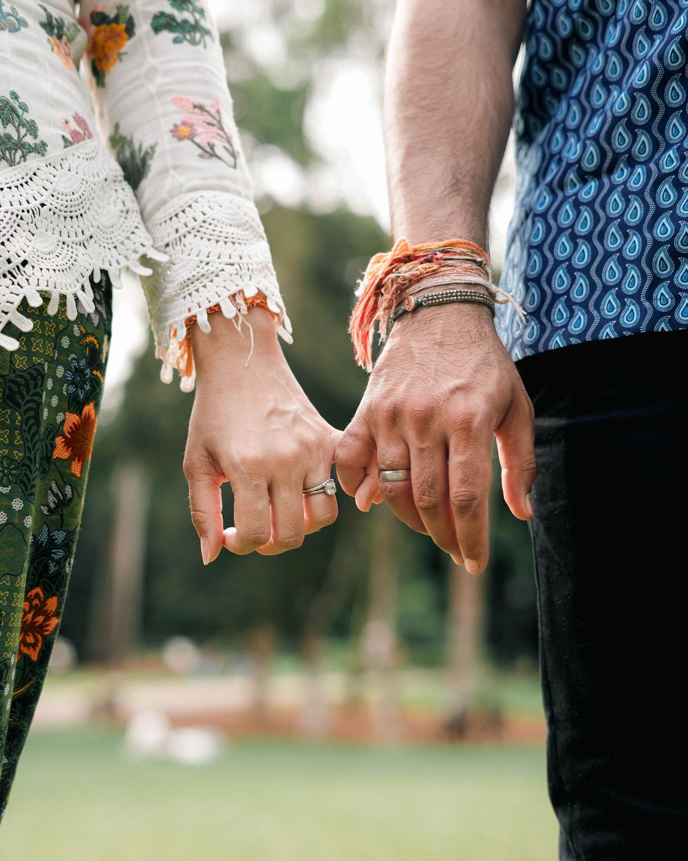 Two hands with wedding rings holding each other affectionately in a garden setting with soft lighting.