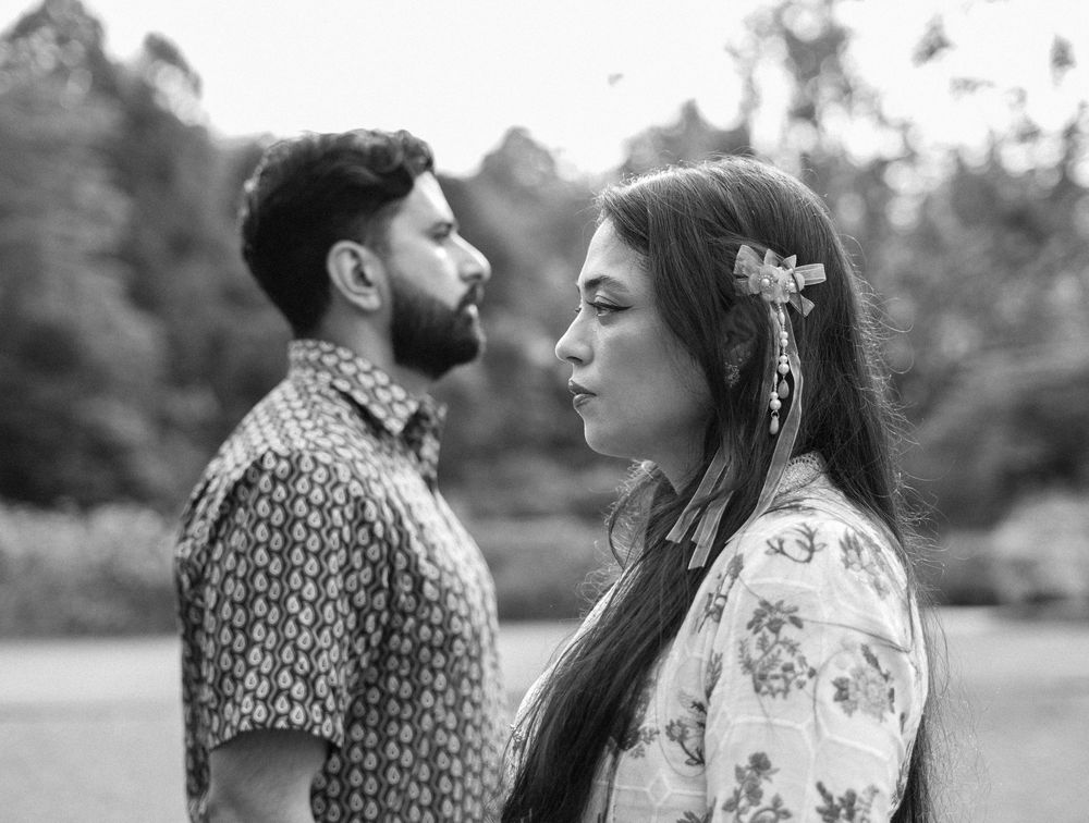 A romantic black and white photo of a couple in patterned shirts standing close together outdoors.