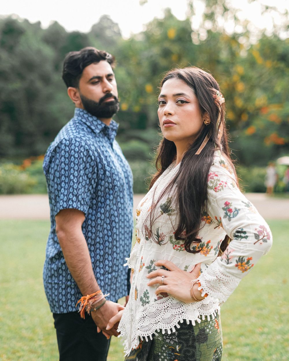 Couple poses together outdoors in contrasting outfits of blue pattern and white lace against a natural garden setting.