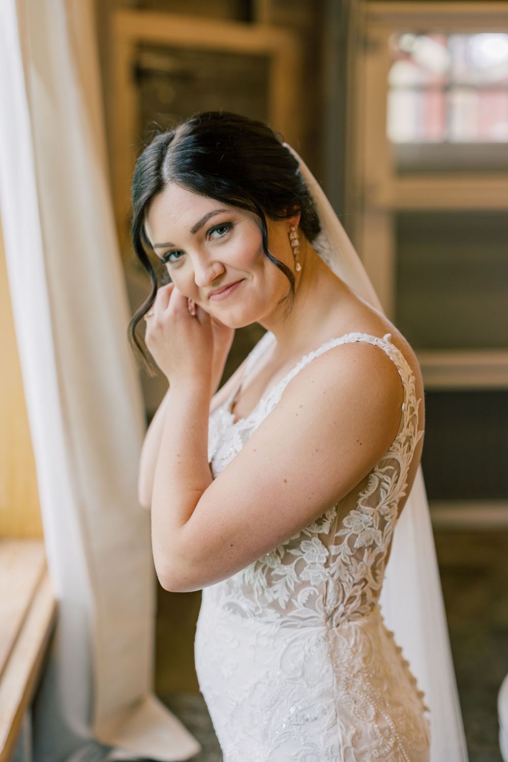 A bridal portrait series showing a woman in a delicate lace wedding gown and veil in warm lighting.