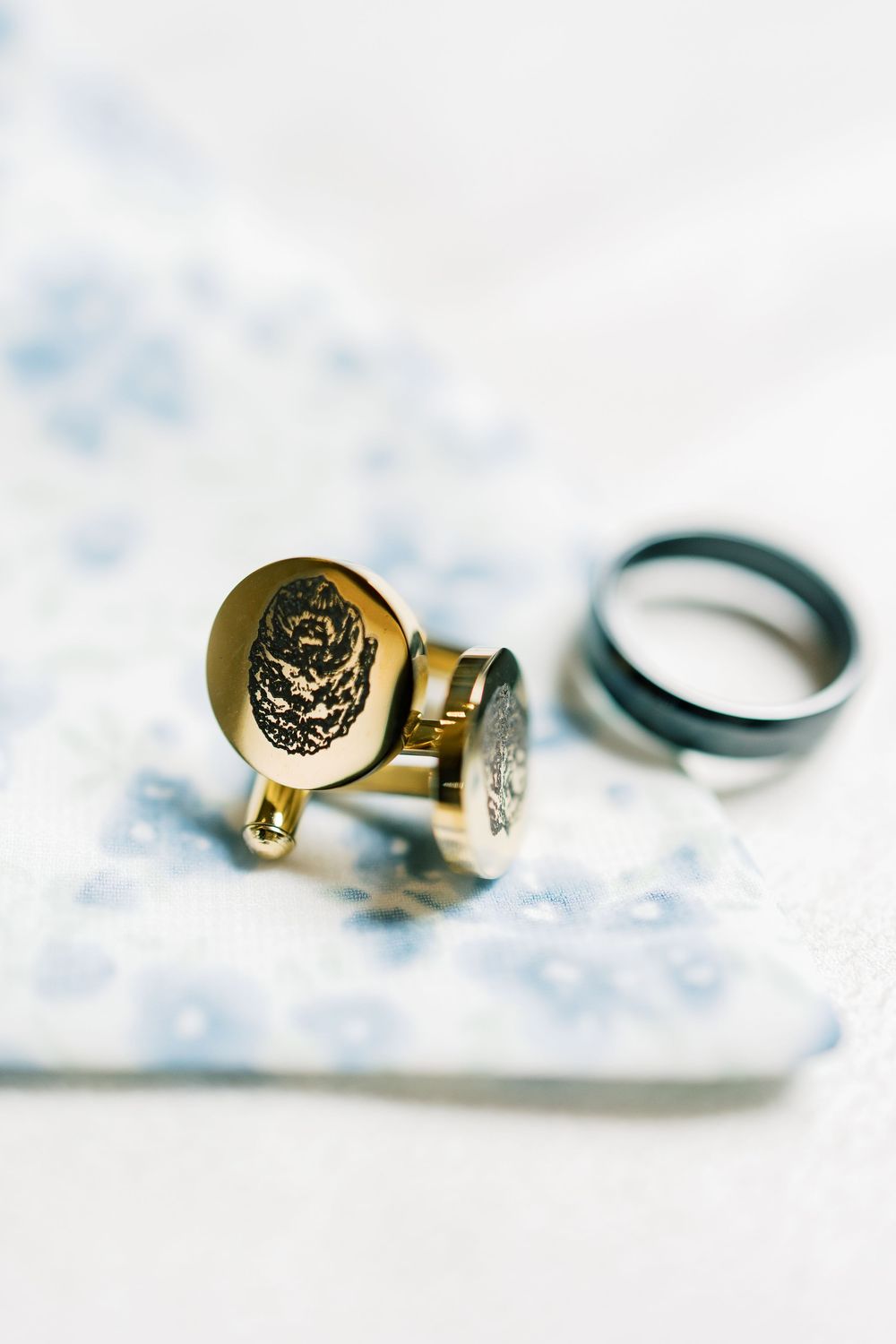 Gold cuff links with ornate designs and embellishments arranged on light blue floral fabric.