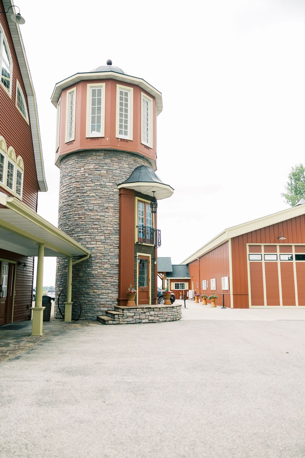 Stone and brick tower with circular observation room rises next to red barn buildings in rustic farmhouse setting.