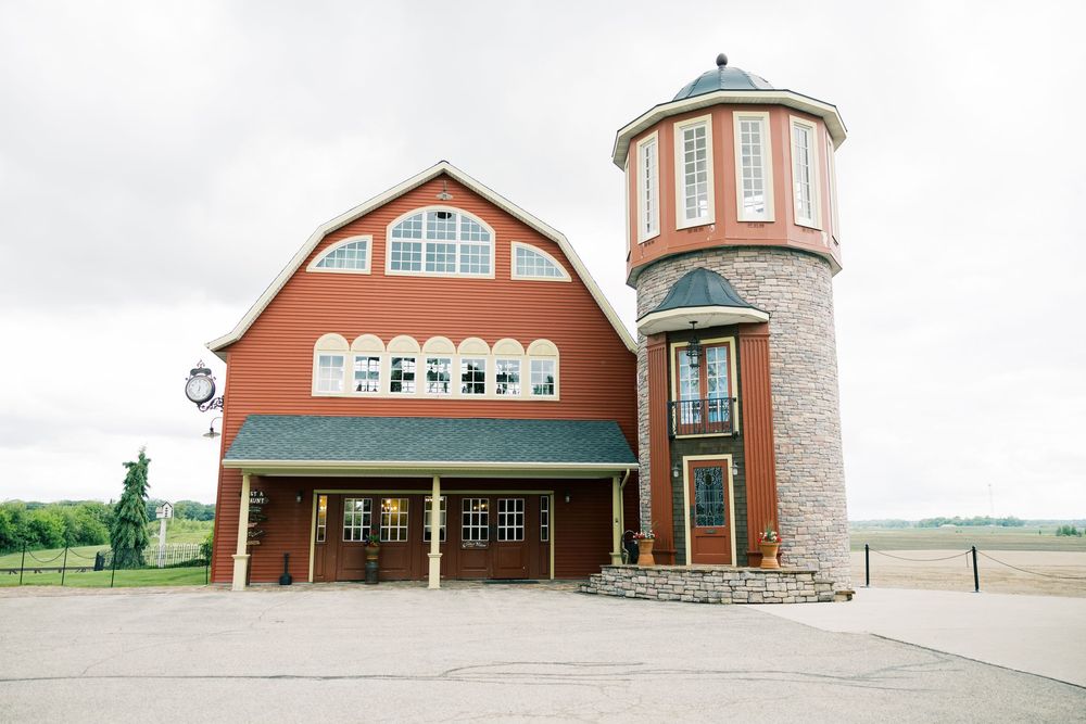 Panoramic view of a rustic red barn style wedding venue with white siding and large windows in a rural setting.