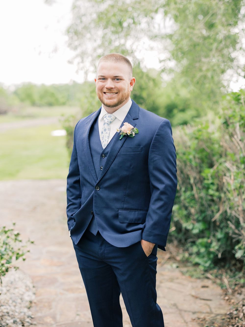 Men in navy and grey suits pose for wedding portraits in a natural outdoor setting.