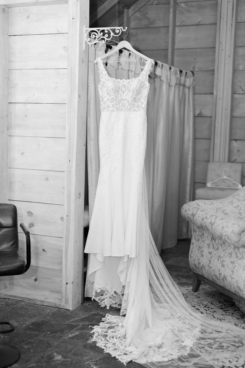 Wedding dress hanging in rustic cabin room showing delicate lace details and train.